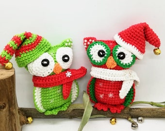 May include: Two crocheted owl ornaments, one green with a red scarf and a red and white hat, the other red with a white scarf and a red hat. Both owls have white eyes and are sitting on a branch.