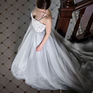 May include: A woman wearing a light gray tulle wedding dress with a lace bodice. She is standing on a staircase with a wooden railing.