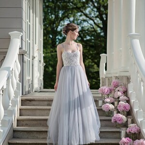 May include: A woman in a light blue tulle wedding dress with a white lace bodice stands on a set of stairs decorated with pink peonies and candles.