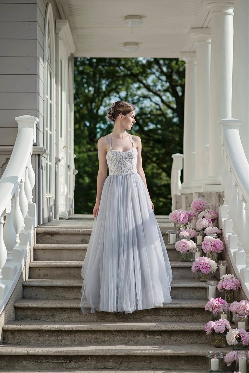 May include: A woman in a light blue tulle wedding dress with a white lace bodice stands on a set of stairs decorated with pink peonies and candles.