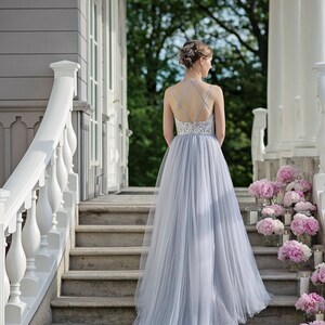 May include: A woman in a light blue tulle gown with a lace bodice walks down a set of stone stairs. The stairs are lined with pink peonies and candles.