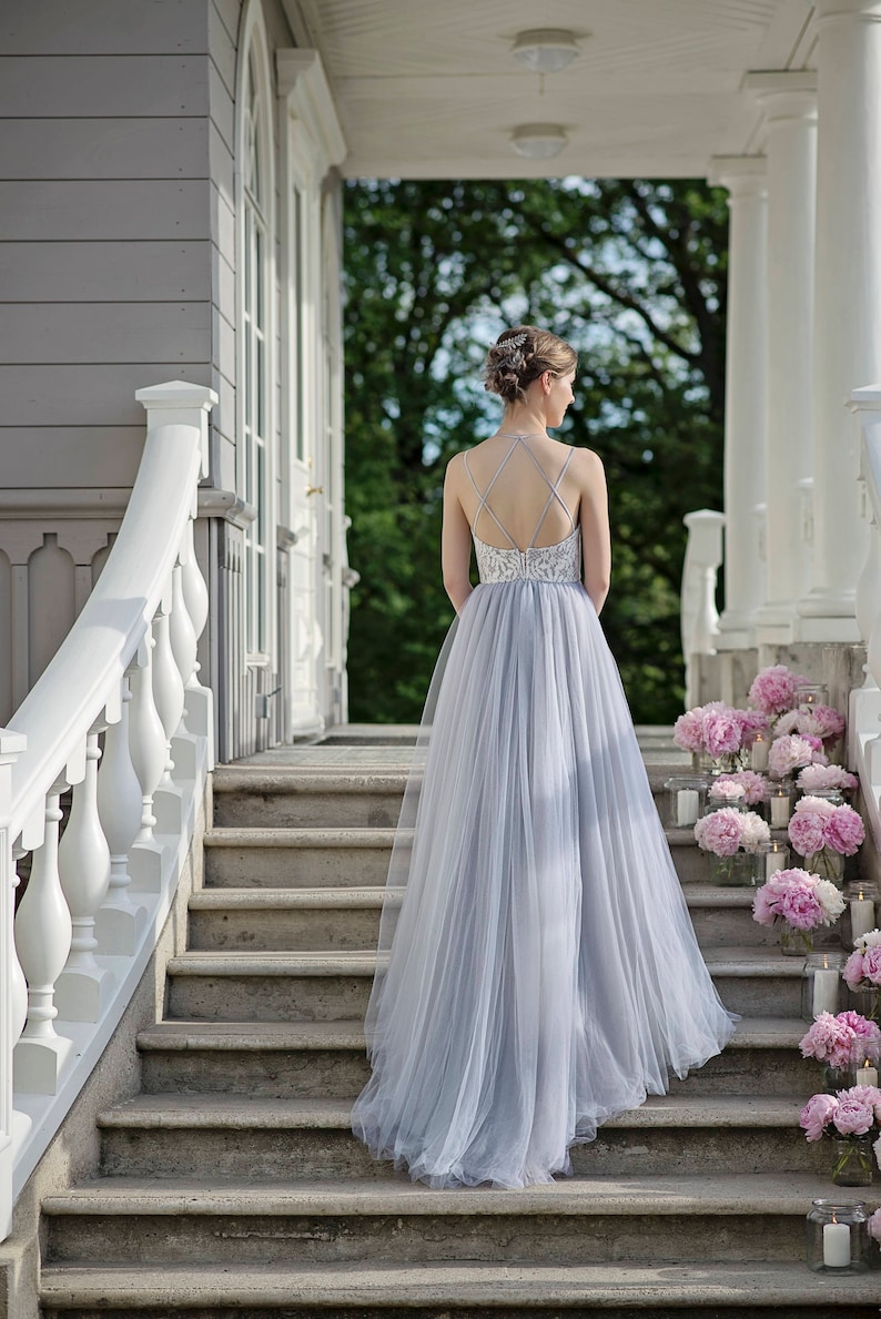 May include: A woman in a light blue tulle gown with a lace bodice walks down a set of stone stairs. The stairs are lined with pink peonies and candles.