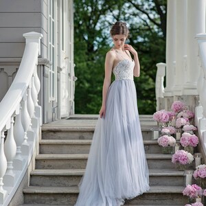 May include: A woman in a light blue tulle wedding dress with a white lace bodice stands on a set of stone steps decorated with pink peonies and candles.