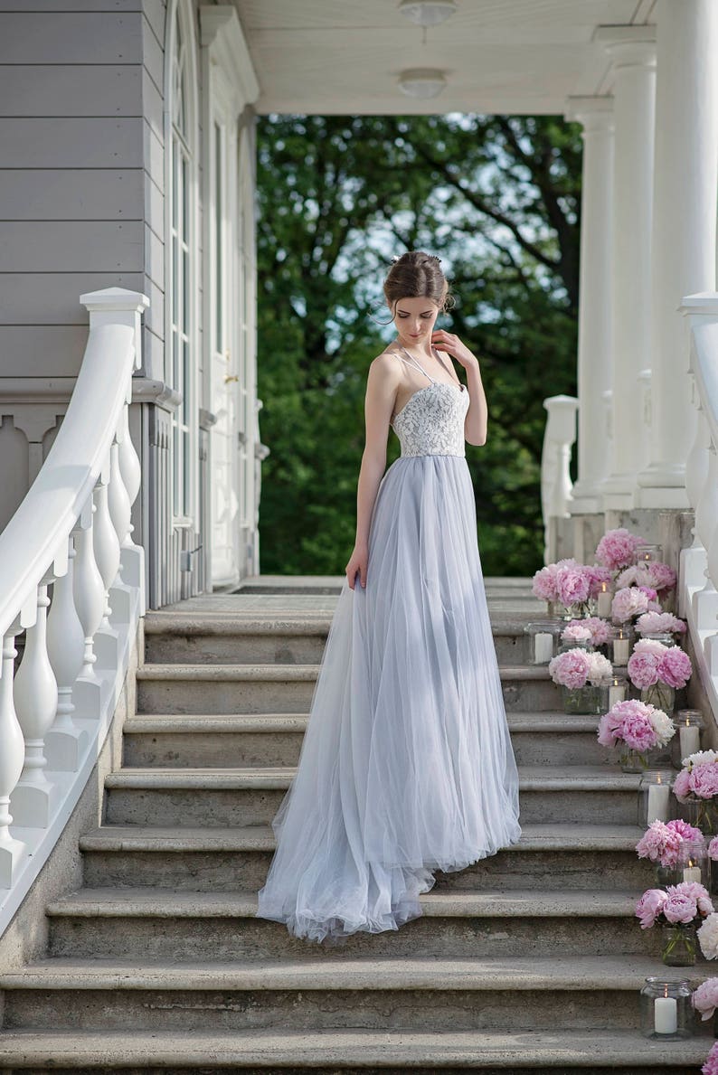May include: A woman in a light blue tulle wedding dress with a white lace bodice stands on a set of stone steps decorated with pink peonies and candles.