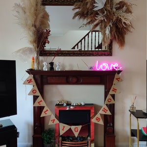 May include: A decorated fireplace with a mirror, dried floral arrangements, and a banner that reads "NOLA & SHONA". A neon sign displays the word "love". Decorative items include small figurines and a miniature bicycle.