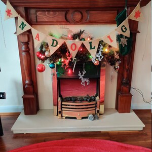 May include: A decorated fireplace with a banner that reads "NADOLIG". The fireplace is adorned with Christmas ornaments, lights, and a green stocking. The mantelpiece is made of dark wood, and the hearth is white.