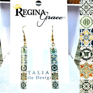 May include: Gold-tone dangle earrings with rectangular pendants featuring a colorful tile design. The earrings are displayed on a white card with the text "Regina Grace" and "ITALIA Tile Design".