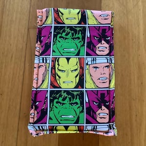 May include: A rectangular fabric pouch featuring a repeating comic book print of Marvel superheroes including Iron Man, the Hulk, Thor, and Hawkeye. The design consists of colorful square panels with bold black outlines on a white background.