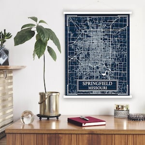 Pode incluir: Uma impressão de mapa de Springfield, Missouri, de cor azul marinho, com linhas brancas mostrando as ruas e uma borda branca. O texto "Springfield Missouri" está em um retângulo branco na parte inferior do mapa.