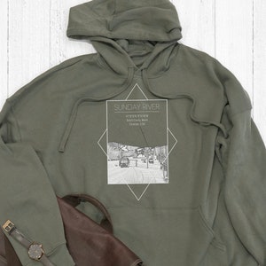 Könnte beinhalten: Ein grüner Kapuzenpullover mit dem Text "SUNDAY RIVER" und einer Grafik eines Skilifts in einer Diamantform. Der Text unter der Grafik lautet "ARROWHEAD'S" "First Chair Maine" "Mountain Life".