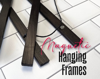 May include: Black wooden magnetic hanging frames with a black string attached. The frames are on a white tiled surface. The text "Magnetic Hanging Frames" is written in pink letters below the frames.