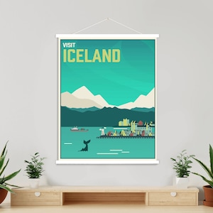 May include: A travel poster with the words "VISIT ICELAND" in yellow letters. The poster depicts a coastal scene with mountains, a whale tail, and colorful buildings. The poster is displayed on a white frame.