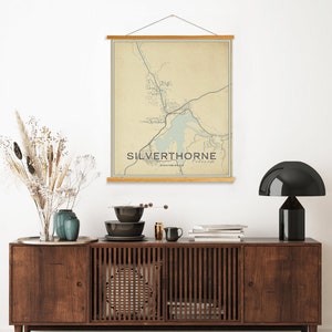 Pode incluir: Uma impressão de mapa de estilo vintage de Silverthorne, Colorado, com fundo bege e linhas azuis. O mapa é emoldurado com uma moldura de madeira e pendurado em uma parede branca acima de uma cômoda de madeira.