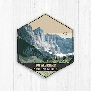 May include: A vintage-style illustration of Voyageurs National Park in Minnesota. The image features a mountain range with a lake in the foreground and two birds flying overhead. The text "Voyageurs National Park" is printed below the image.