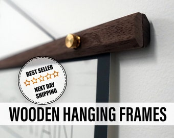 May include: Wooden hanging frame with a dark brown wooden bar and a brass-colored knob. The frame is hanging on a white wall. The text "Wooden Hanging Frames" is displayed at the bottom of the image.