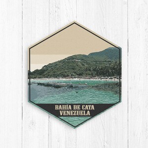 May include: A vintage travel poster with a hexagonal design featuring a scenic view of a beach with boats in the water and a lush green mountain in the background. The text "BAHIA DE CATA VENEZUELA" is at the bottom of the poster.