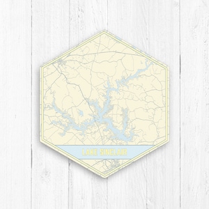 Può includere: Una mappa esagonale del lago Sinclair, Georgia, con un bordo blu chiaro e giallo e il testo "LAKE SINCLAIR" in uno stendardo blu chiaro.