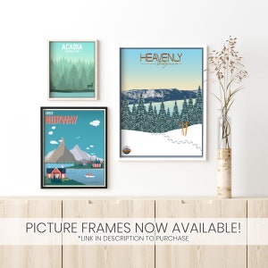 May include: Three framed travel posters with a minimalist design. The posters feature illustrations of Acadia National Park, Heavenly California, and Norway. The posters are displayed on a white wall with a wooden shelf below.