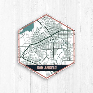 Op de afbeelding: Een zeshoekige kaartprint van San Angelo, Texas, met een witte achtergrond, zwarte lijnen en een blauwe rivier. De kaart is omgeven door een donkerblauwe rand met de naam van de stad in witte tekst. De rand is omlijnd met een lichtroze kleur.