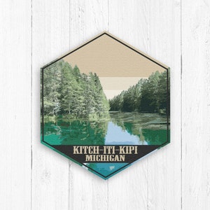 May include: A hexagonal shaped vintage travel poster with a green, blue, and beige color scheme. The poster features a scenic view of a lake surrounded by trees. The text on the poster reads "Kitch-iti-kipi Michigan".