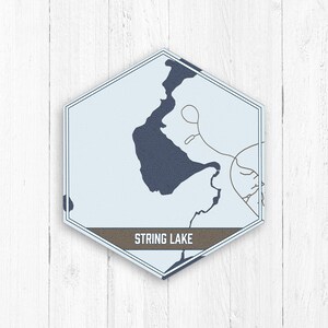 May include: A blue and white hexagon-shaped map of String Lake with the text "String Lake" in brown lettering.