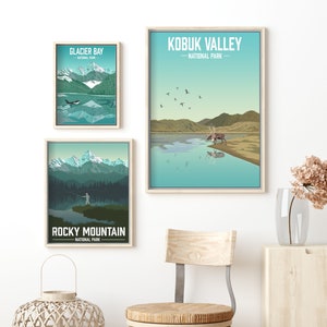 May include: Three framed prints of national parks in the United States. The top print is of the Kobuk Valley National Park in Alaska, featuring a caribou standing in a lake with mountains in the background. The middle print is of Glacier Bay National Park in Alaska, featuring a whale swimming in a lake with mountains in the background. The bottom print is of Rocky Mountain National Park in Colorado, featuring a person fishing in a lake with mountains in the background.