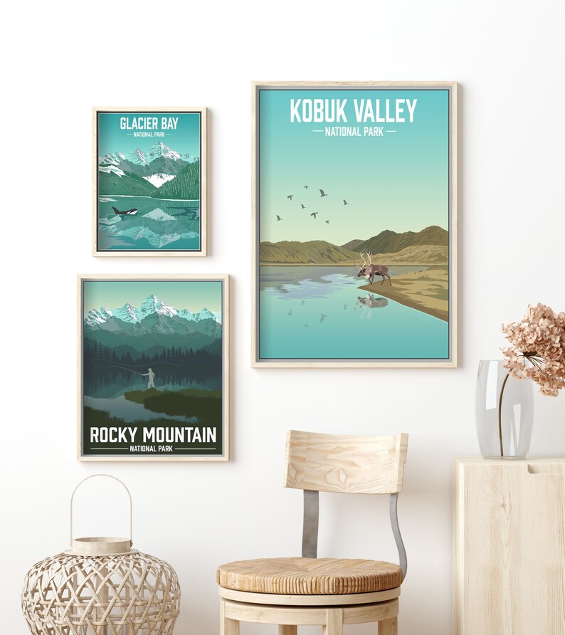 May include: Three framed prints of national parks in the United States. The top print is of the Kobuk Valley National Park in Alaska, featuring a caribou standing in a lake with mountains in the background. The middle print is of Glacier Bay National Park in Alaska, featuring a whale swimming in a lake with mountains in the background. The bottom print is of Rocky Mountain National Park in Colorado, featuring a person fishing in a lake with mountains in the background.