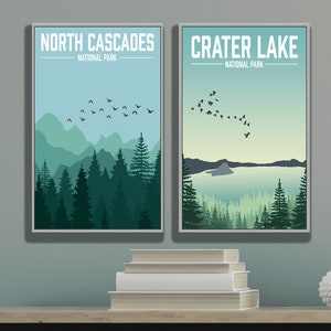 May include: Two framed posters with a minimalist design. The poster on the left features a mountain range with a flock of birds flying overhead. The text on the poster reads "North Cascades National Park". The poster on the right features a lake with a small island in the middle. The text on the poster reads "Crater Lake National Park".