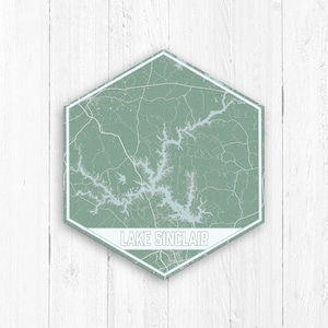 Può includere: Un cartello esagonale verde e bianco con una mappa del lago Sinclair, Georgia. Il cartello ha un bordo bianco e il testo "LAKE SINCLAIR" in lettere bianche.