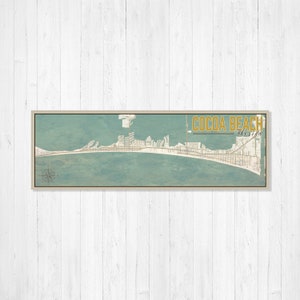 Puede incluir: Un mapa de estilo vintage de Cocoa Beach, Florida, con una combinación de colores azul y verde. El mapa muestra la costa y las calles de la ciudad. El texto "COCOA BEACH Florida" está impreso en dorado en la parte superior del mapa.