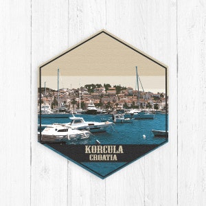 May include: A hexagonal travel sticker with a photo of a harbor in Korcula, Croatia. The sticker features a blue and beige color scheme with the text "Korcula Croatia" in a dark blue banner.