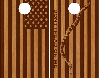 May include: Two wooden cornhole boards with a red, white, and blue American flag on one side and a brown snake with the words "Don't Tread On Me" on the other side.