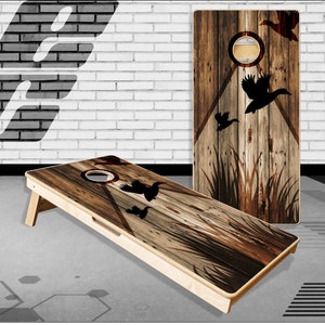May include: A wooden cornhole board with a rustic wood grain design and silhouettes of flying ducks. The board has a brown, black, and white color scheme.
