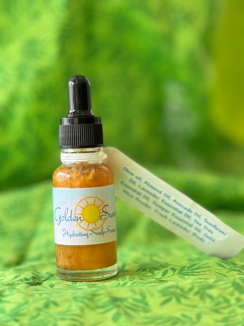 May include: A small glass bottle of Golden Sun Hydrating Scalp Serum with a black dropper. The label features a sun graphic and the product name. A white ingredient list is next to the bottle. The serum is a golden color.