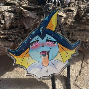 Puede incluir: Un collar con un colgante de acrílico transparente de una criatura azul, amarilla y blanca con una expresión facial estilizada. El colgante cuelga de un cordón negro adornado con cuentas azules, blancas y negras, con cierres de metal plateado.