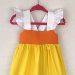 May include: A yellow and orange dress with white straps and ruffled sleeves. The dress has a criss-cross back and a gathered skirt.