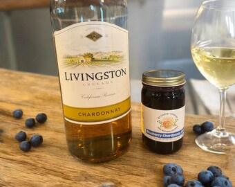 May include: A bottle of Livingston Cellars California Reserve Chardonnay wine, a jar of blueberry Chardonnay jam, and a glass of white wine with blueberries scattered on a wooden surface.