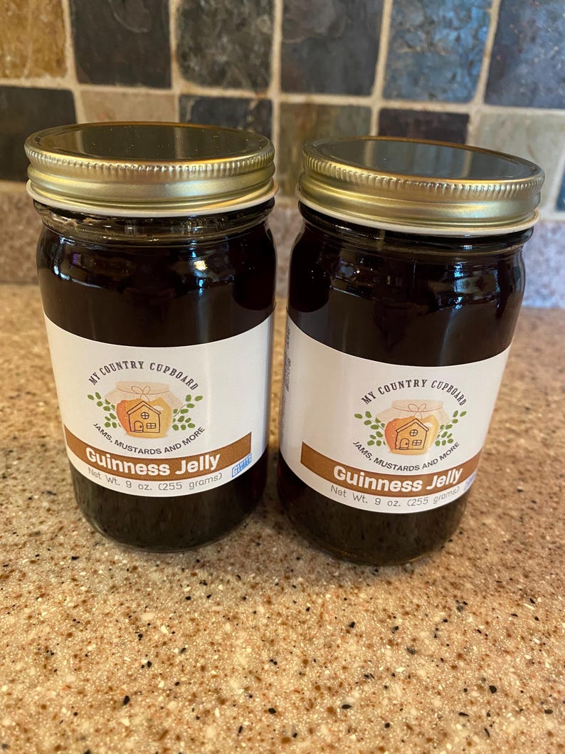 May include: Two glass jars of Guinness Jelly with gold lids and white labels. The labels read "My Country Cupboard" and "Guinness Jelly". Each jar contains 9 oz. (255 grams) of jelly.