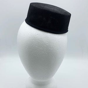 Puede incluir: Un sombrero de malla negra con un ala ancha. El sombrero está sentado en una cabeza de poliestireno blanco.