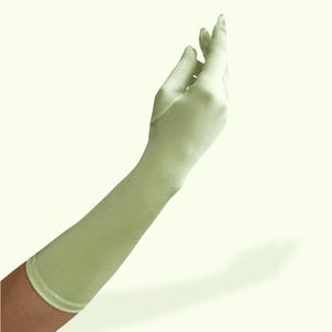 May include: A long, light sage green glove with a smooth, satin-like finish that extends past the wrist and covers the forearm. The glove features a fitted design that contours to the shape of the hand and arm, ending in a clean, hemmed edge.
