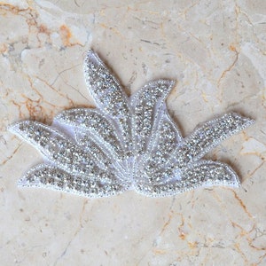 May include: A white flower-shaped applique with silver rhinestones. The applique is made of fabric and has a delicate, feminine design.