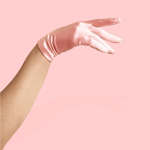 May include: A hand wearing a pink satin glove, with the fingers extended and the palm facing up.
