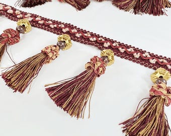 Peut inclure: Garniture de franges bordeaux et dorées avec des perles décoratives. La garniture présente un motif répété de zigzags et de petits motifs floraux.