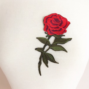 May include: Red embroidered rose with green leaves and stem. The rose is a single bloom with a dark red center and light red petals. The leaves are a dark green color.