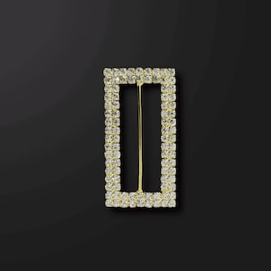 May include: A gold-toned rectangular buckle with a clear rhinestone border. The buckle has a metal pin in the center.