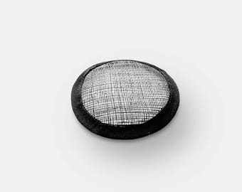 May include: A black and silver fascinator hat with a circular shape. The hat features a woven silver mesh top and a black, rounded brim. The design is simple and elegant, suitable for formal events or special occasions.