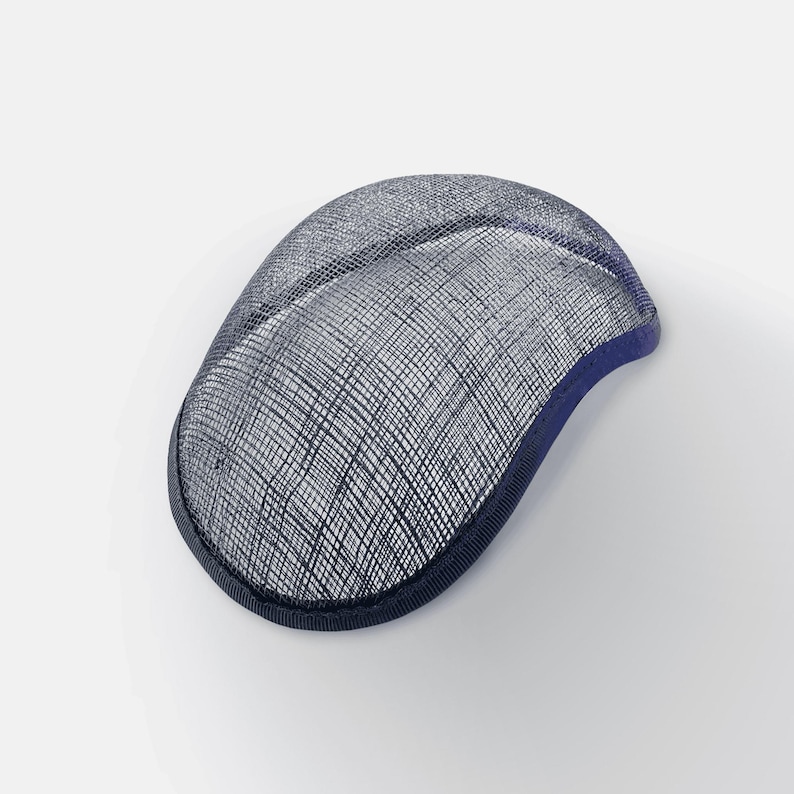 K&ouml;nnte beinhalten: Eine marineblaue Sinamay-Hutbasis, eine Art Stroh, das f&uuml;r die Hutmacherei verwendet wird, mit einer gewebten Textur. Die Basis ist oval geformt und hat einen leicht gekr&uuml;mmten Rand.