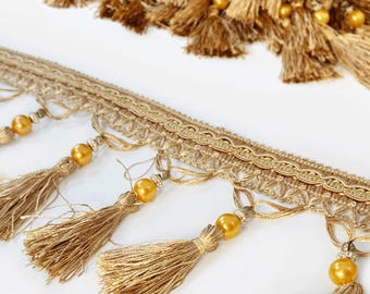 Peut inclure: Garniture de glands dorés avec perles décoratives. La garniture présente un motif tissé avec des glands pendants et des perles dorées. Les glands sont faits d'un matériau doux et fluide. La garniture convient à divers projets d'artisanat et de design.