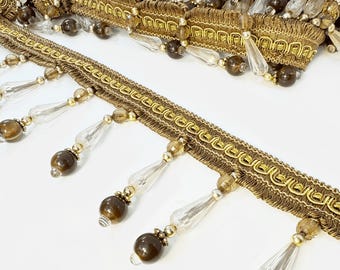Peut inclure: Frange à perles avec bordure dorée, composée de perles en verre brun et transparent. La frange présente un motif répétitif de bordure dorée et de perles.