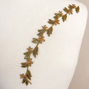 May include: Gold and green embroidered trim featuring a vine and flower design. The trim is ideal for adding a touch of elegance to any project.